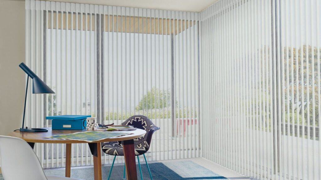 Modern workspace with vertical blinds, desk lamp, and colorful chair offering a relaxing and functional office area, perfect for working or reading.